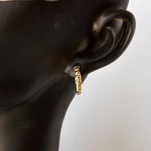 Load image into Gallery viewer, A close-up of a textured gold huggie hoop earring worn on a black mannequin ear, set against a plain light gray background. Talayee Fine Jewelry's Atousa Huggie Hoop Earrings.