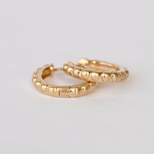Load image into Gallery viewer, A pair of small gold hoop earrings with a textured, beaded outer edge, displayed on a plain light gray background. Talayee Fine Jewelry's Atousa Huggie Hoop Earrings.