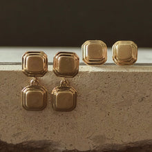 Load image into Gallery viewer, Pair of gold square geometric earrings on a textured surface with a dark background