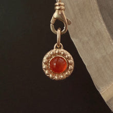 Load image into Gallery viewer, A close-up of medallion pendant set with a carnelian cabochon centered to a raised textured border against a black background with draped fabric. Talayee Fine Jewelry's Atousa Medallion Pendant.