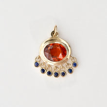Load image into Gallery viewer, A 14k gold persepolis pendant featuring a large oval faceted orange-red garbet in the center, with five small dangling blue sapphire gemstones along the bottom curved row, set against a plain light background.