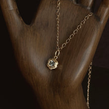 Load image into Gallery viewer, Gold necklace with a floral shaped pendant set with a spinel on a wooden surface