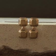 Load image into Gallery viewer, Gold geometric earrings on a textured surface with a dark background