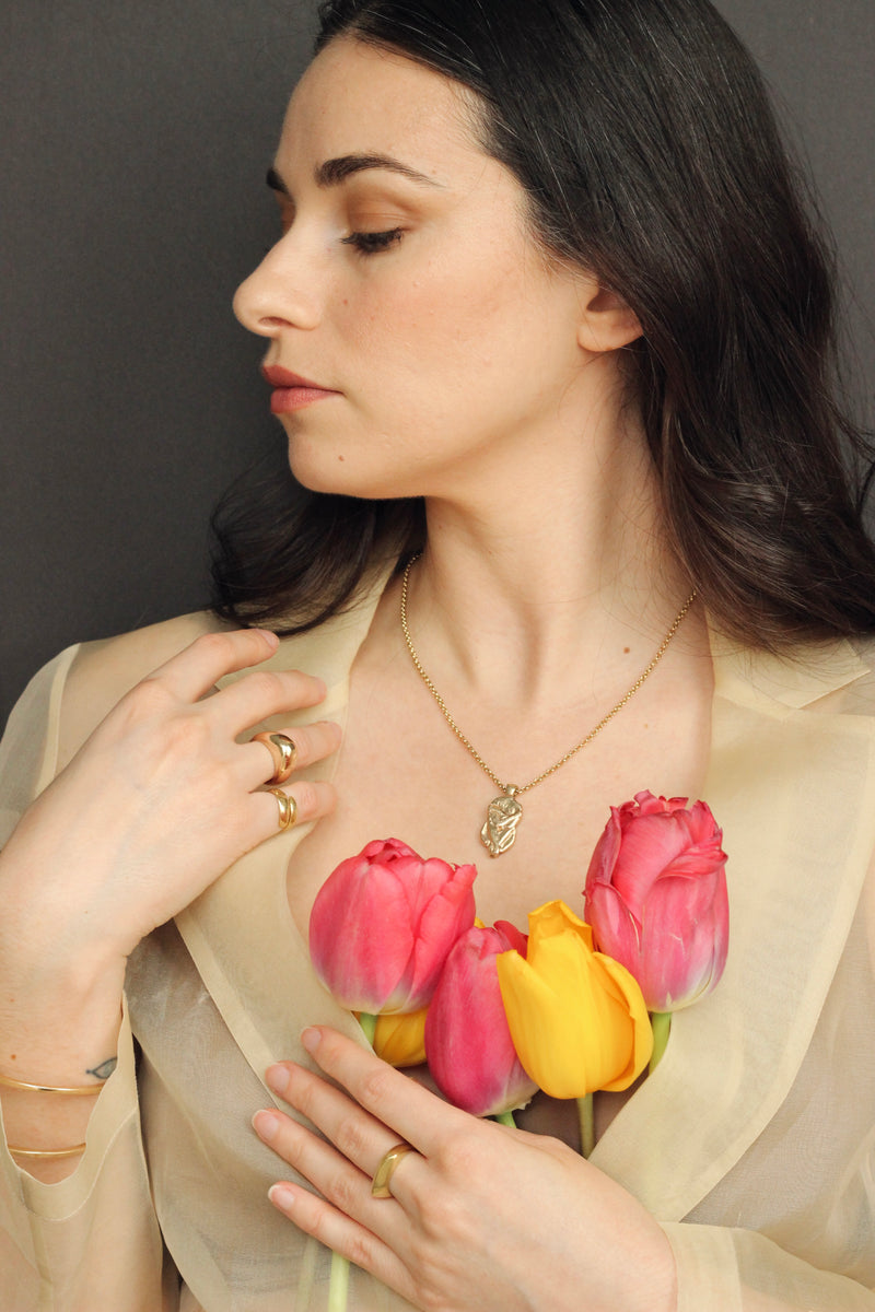14k gold statement ring and 14k gold statement necklace on model with tulips on a black background