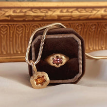 Load image into Gallery viewer, Gold necklace with floral pendants and a gold ring with a floral pink gemstone on a brown velvet cushion, with an ornate wooden box in the background.
