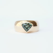 Load image into Gallery viewer, A gold cigar band style ring featuring a trillion cute teal sapphire in a bezel setting, photographed against a clean white background.
