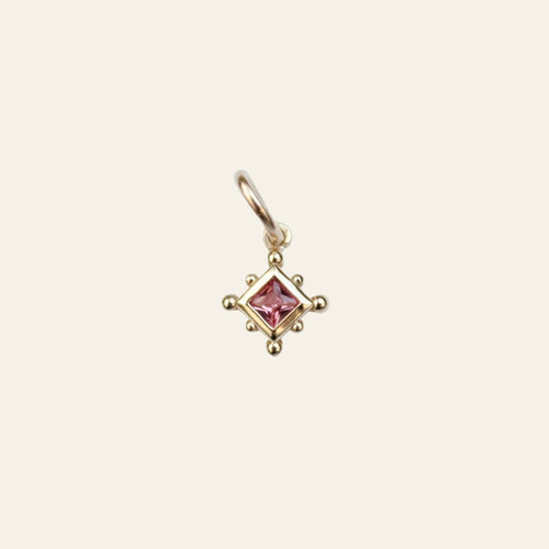 Gold charm pendant with a pink spinel on a light gray background