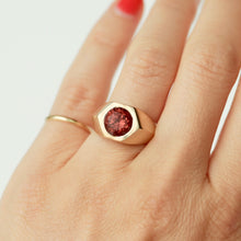 Load image into Gallery viewer, A gold signet-style ring with a hexagonal bezel set with a round malaya garnet, shown worn on a person's hand against a clean white background.
