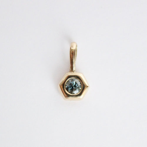 14k yellow gold charm set with a round gray spinel on a light gray background