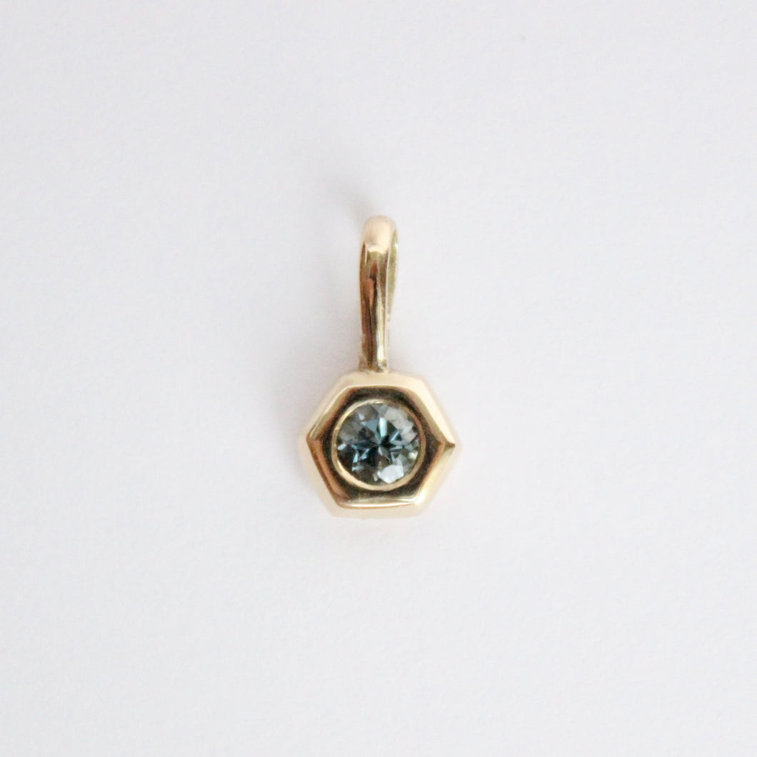14k yellow gold charm set with a round gray spinel on a light gray background