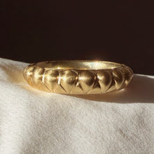 Load image into Gallery viewer, A textured gold band ring with a raised pear shaped pattern, resting on a white fabric surface under warm, directional light. Talayee Fine Jewelry's Atousa Ring.
