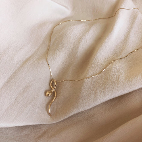 14k Gold snake charm necklace on white background. 